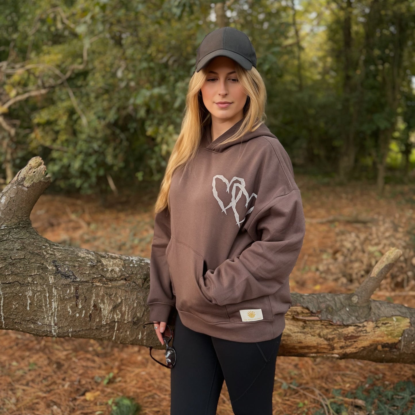 Person wearing a brown hoodie with a logo in a forest setting
