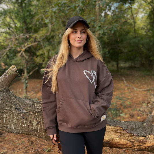 Woman wearing a brown hoodie with a logo in a forest setting