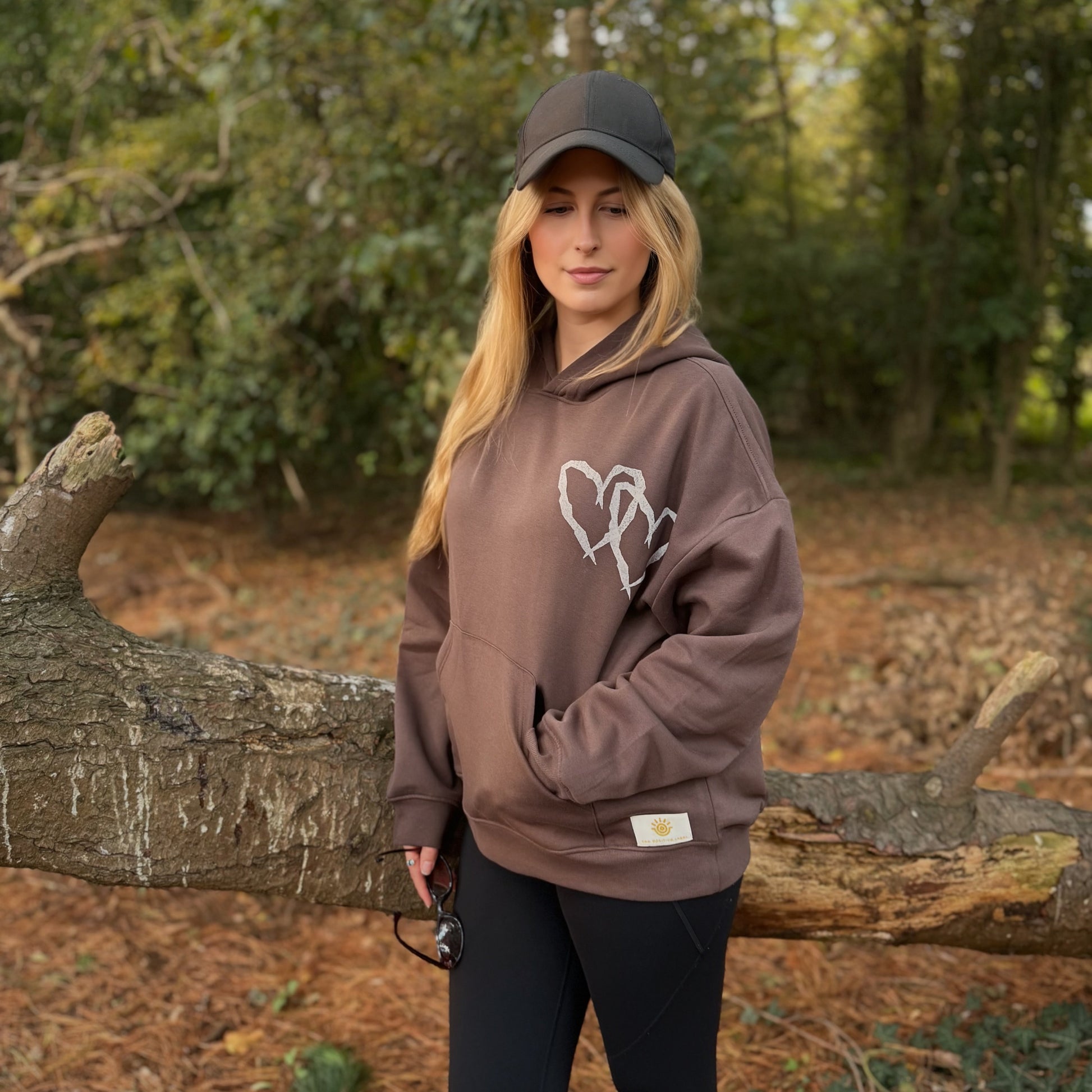 Person wearing a brown hoodie with a logo in a forest setting