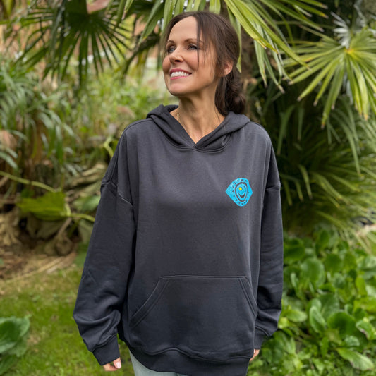 Woman wearing a navy hoodie with a logo, standing in a garden.