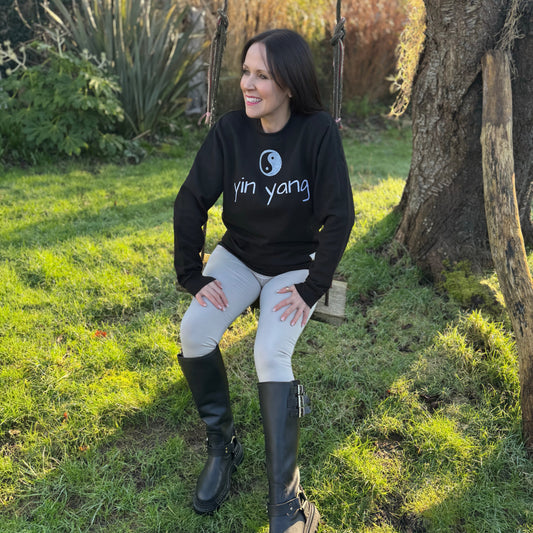 A woman sitting on a swing wearing a black sweatshirt with the text 'yin yang' and a corresponding symbol on the front.